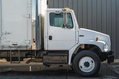 Profile view of white 2000 Freightliner FL80 mud truck featuring steel box body, heavy-duty chassis, and steerable axle.