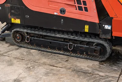 2016 Ditch Witch JT25 rubber track undercarriage close-up, worn tread with tie-down D-rings, safety decals visible on orange frame