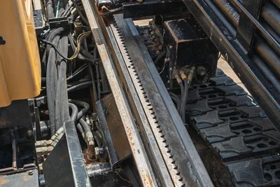 Vermeer D24x40 S3 HDD drill carriage rack gear and hydraulic hose bundle with rubber track visible, surface wear present.