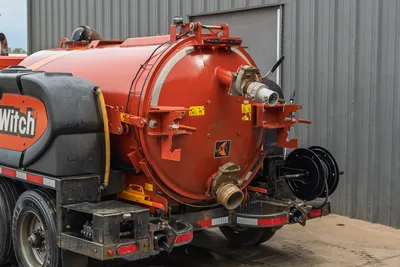 2023 Ditch Witch HX75 rear vacuum tank view showing rear door, discharge manifold, hose reel, cam-lock fittings, and safety decals