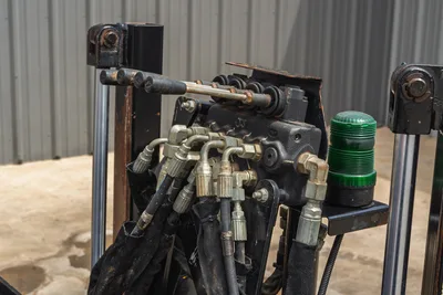 Close-up of Ditch Witch JT10 hydraulic control bank with levers, steel fittings, hoses, and green signal beacon.