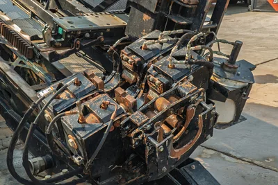 2017 Vermeer D100x140 S3 carriage assembly close-up showing vise jaws, hydraulic lines, and drive components with heavy field wear.