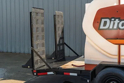 2023 MAXX-D C6X trailer rear view showing diamond-plate fold-down ramps, Ditch Witch mud tank, dual axle, and red hose connection