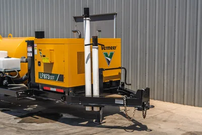 Vermeer LP873SDT vacuum excavator trailer hitch end, yellow power unit enclosure, exhaust stack, safety labels, tongue with safety chains visible