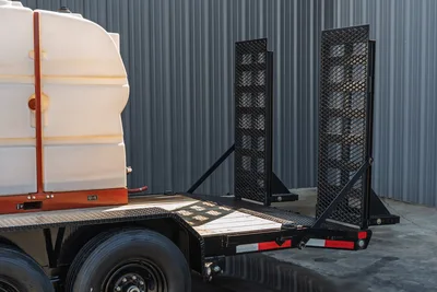 2023 MAXX-D C6X trailer rear view showing diamond-plate deck, folded mesh ramps, tandem axle, and white poly water tank mounted forward