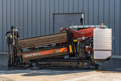 Ditch Witch JT10 HDD rig, side view showing tracked carrier, drill pipe bundle, red power unit, and white fluid tank assembly
