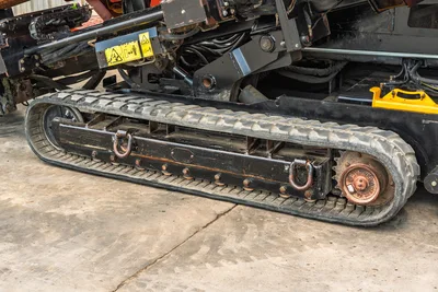 2021 Ditch Witch JT28 rubber track close-up showing drive sprocket, tie-down shackles, hydraulic lines, and yellow safety decals