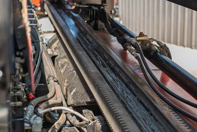 2022 Ditch Witch JT20 drill frame rack-and-pinion gear track, hydraulic hoses, and vise assembly, close-up side angle