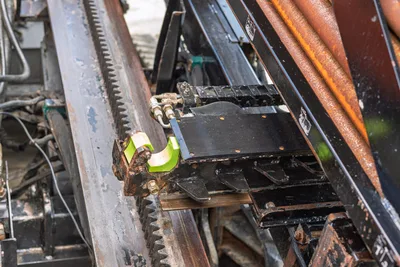 2021 Ditch Witch JT28 drill frame close-up showing rack-and-pinion carriage, vise assembly with green jaw, hydraulic lines, wear from use.