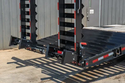 Behnke FB8X30SDPT-40L trailer rear view showing serrated pipe racks, fold-down ramps, red reflectors, and Behnke branding plate.