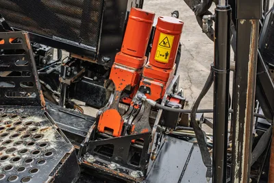 Ditch Witch JT24 vise assembly close-up, dual orange hydraulic pipe vises with wear, safety decal, hydraulic lines, and steel frame visible.