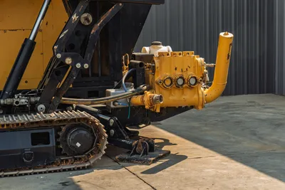 2017 Vermeer D100x140 S3 mud pump close-up showing triplex pump, hydraulic lines, rubber track, and leveling jack pad
