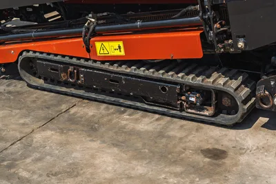 2021 Ditch Witch JT20 rubber track close-up showing hydraulic drive motor, track frame, safety decal, and orange mainframe
