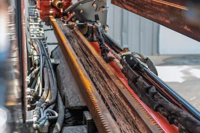 2023 Ditch Witch JT20 drill frame close-up showing rack-and-pinion gear track, hydraulic hoses, and carriage assembly with wear from use.