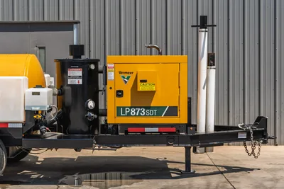Vermeer LP873SDT vacuum excavator trailer, side view showing yellow engine enclosure, black debris tank, standpipe, and pintle hitch with safety chains