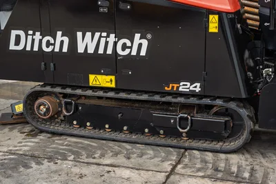 2024 Ditch Witch JT24 HDD drill close-up of rubber track undercarriage, black engine enclosure with safety decals, drill pipe visible