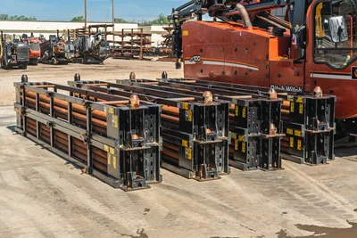 Ditch Witch JT100 Mach 1 drill pipe racks with 3.5" HDD pipe, worn black steel frames, copper-threaded joints, rig cab visible