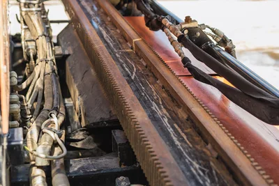 Close-up of Ditch Witch JT20 rack and pinion gear system, hydraulic hoses, and drill frame rails in clean condition.