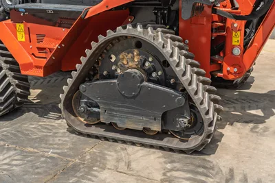 2024 Ditch Witch RT125Q rubber track close-up showing drive sprocket, track rollers, and orange undercarriage frame with safety decals