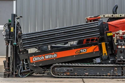 2018 Ditch Witch JT10 HDD drill, side view showing loaded drill pipe rack, rubber tracks, hydraulic lines, orange branding