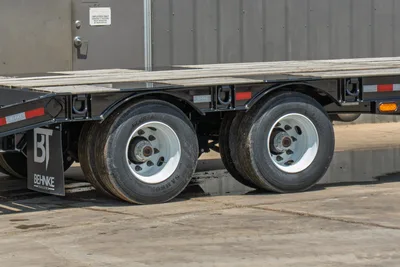 2026 Behnke FB8X30SDPT-40L trailer tandem axle close-up showing Samson tires, white steel wheels, black frame, and wood deck