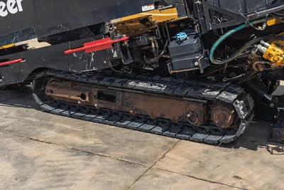 2021 Vermeer D24x40 S3 rubber track close-up showing worn undercarriage, hydraulic lines, fluid reservoir, and red drill pipe sections