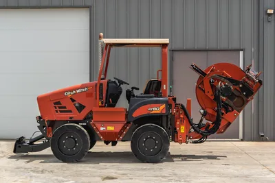 Side profile of 2017 Ditch Witch RT80 utility tractor with rear trencher attachment, open cab, and tires on concrete.
