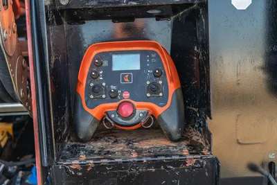 Ditch Witch JT28 remote control unit with orange housing, LCD display, dual joysticks, red e-stop button, showing field wear