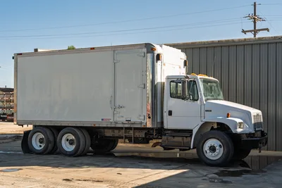 2000 Freightliner FL80 mud truck with white cab, tandem axle, and enclosed Morgan cargo box in profile view.