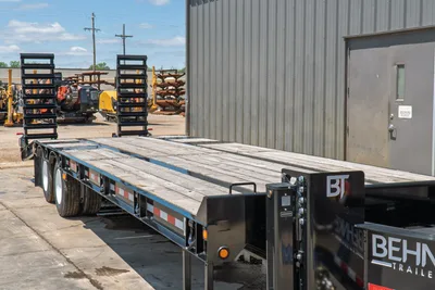 2026 Behnke FB8X30SDPT-40L flatbed trailer, side-rear angle showing wood deck, black steel frame, dual axles, reflective tape, BT branding