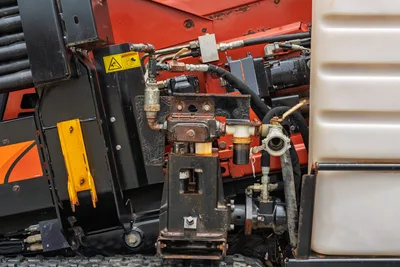 Close-up of Ditch Witch JT10 hydraulic fluid pump system, hoses, and filtration components with visible surface corrosion.