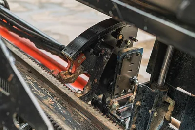 Close-up of Ditch Witch JT20 drill pipe loader mechanism and rack gear assembly showing hydraulic cylinder and carriage.
