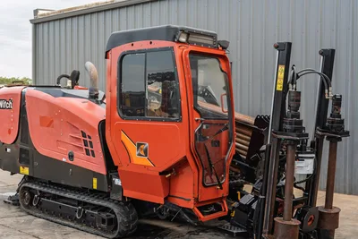 2016 Ditch Witch JT25 HDD drill, passenger-side cab view, enclosed operator cab, rubber tracks, loaded drill pipe rack visible