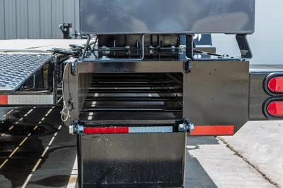 Behnke TBCT2220ET-BT-R trailer rear frame closeup showing pipe rack storage, red reflectors, taillights, diamond-plate deck, and pin-secured receiver
