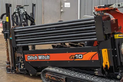 2018 Ditch Witch JT10 HDD drill showcasing side-view, drill pipe rack, steel tracks, hydraulic hoses, and main chassis.