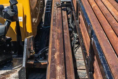 Vermeer D40x55 S3 thrust rack and carriage rail detail with rack-and-pinion gear teeth, hydraulic components, and stacked 2.625" drill pipe