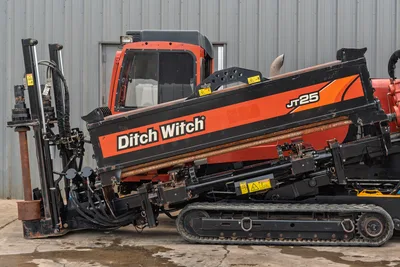 2016 Ditch Witch JT25 HDD drill, passenger-side view showing drill rack, loaded pipe, carriage, rubber tracks, and enclosed cab.
