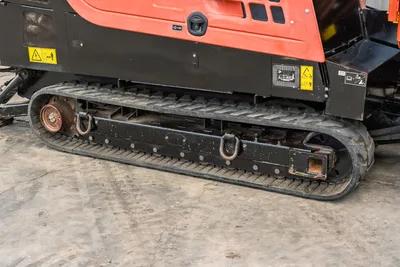 2021 Ditch Witch JT28 rubber track close-up showing D-ring tie-downs, drive sprocket, and red lower chassis with safety decals
