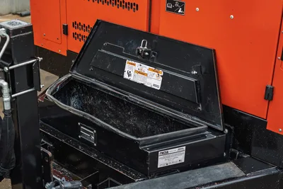2021 Ditch Witch HX50 open lockable black steel toolbox with warning stickers, FMCSA placard, orange engine enclosure behind