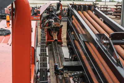 Ditch Witch JT4020 MACH 1 drill carriage, rack-and-pinion drive, pipe rack with drill pipe stacked, and orange engine hood.