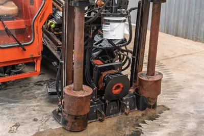 2016 Ditch Witch JT25 drill frame close-up showing anchor posts, vise assembly, hydraulic lines, and fluid bucket, wear-used condition